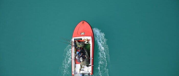 Top view of a red motorboat with fishermen navigating open turquoise waters.